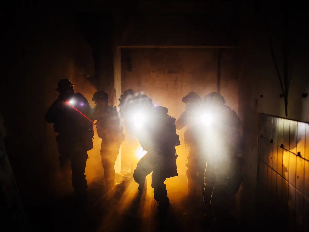 An armed tactical team with lights entering a smoke-filled building.