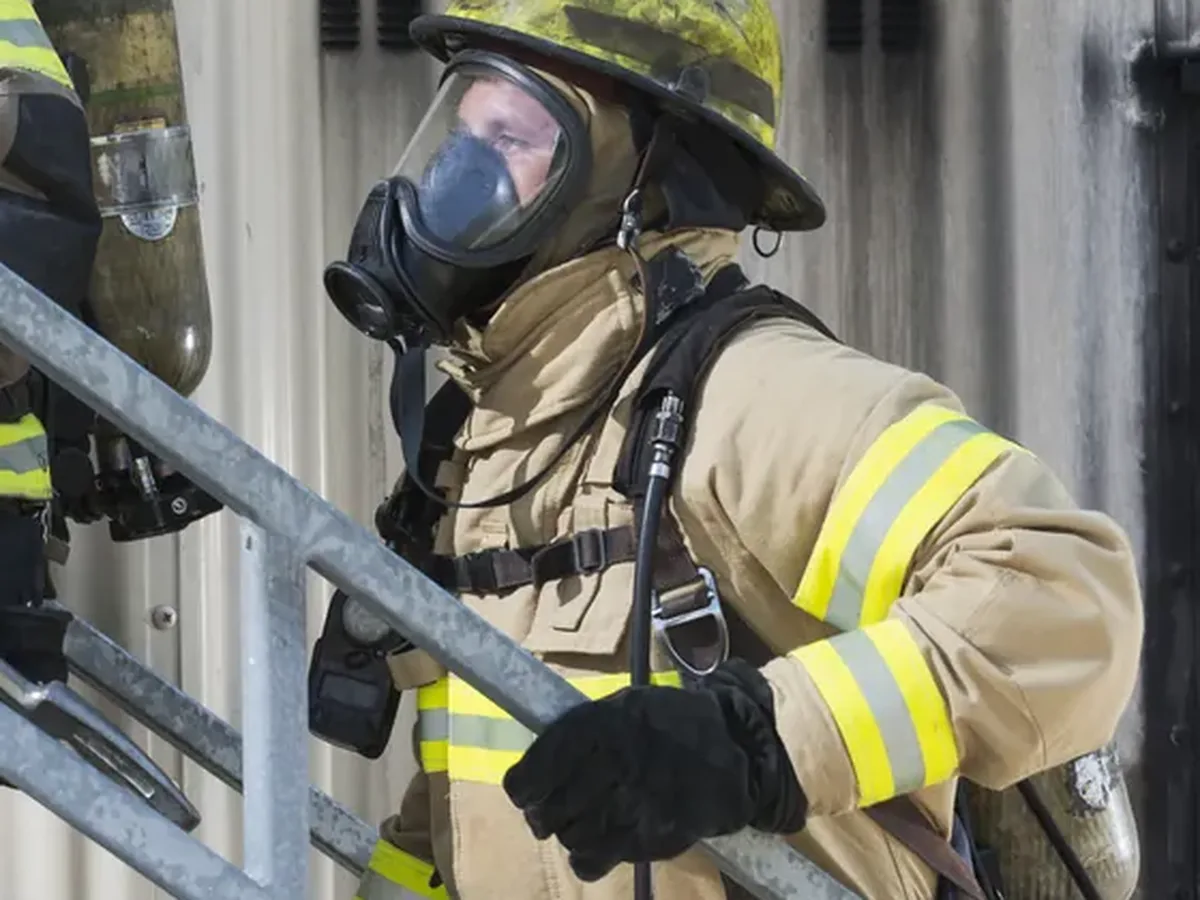 A firefighter in breathing apparatus climbing an exterior steel staircase.