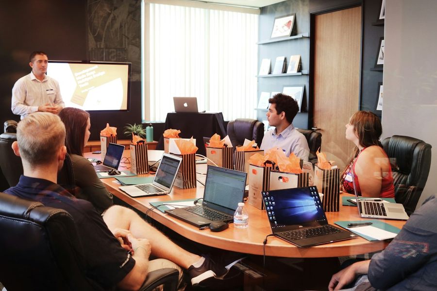 A consultant leading a working session at a table of people with laptops.